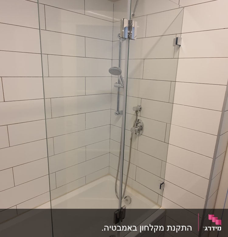 מקלחת עם דלת זכוכית וברז מתכת על קיר אריחים לבנים